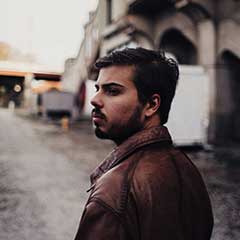 A man in brown jacket standing on street next to buildings.