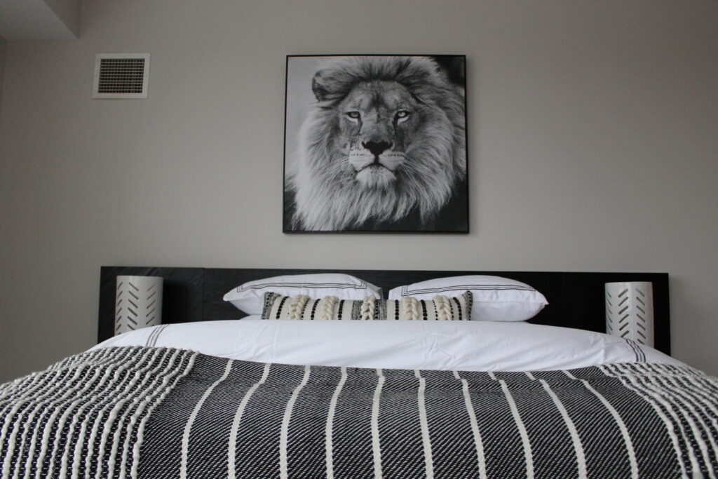 A black and white photo of a lion on the wall above a bed.